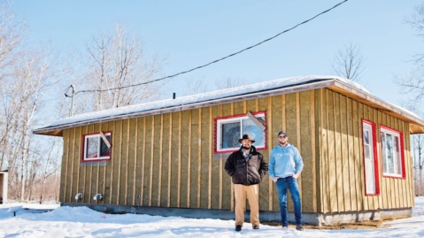 Skownan First Nation two gentleman standing outside of home doing an "outsulation" project.