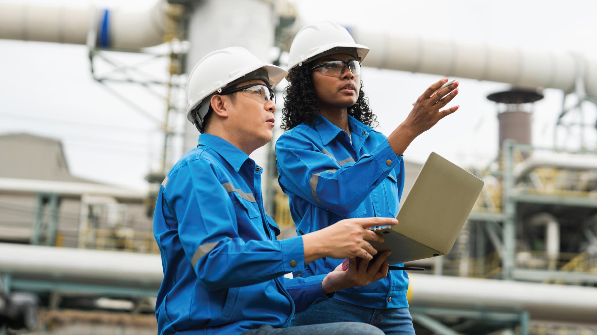 Male and female engineers working using laptop in industrial setting